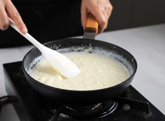 Persona removiendo una bechamel casera en una sartén para preparar brócoli con bechamel al horno