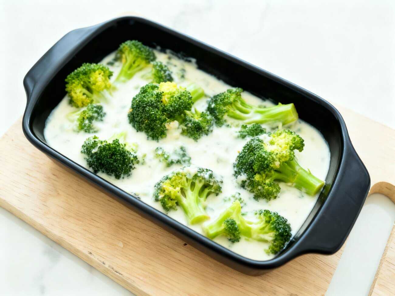 Fuente de horno con ramilletes de brócoli cubiertos con bechamel lista para gratinar