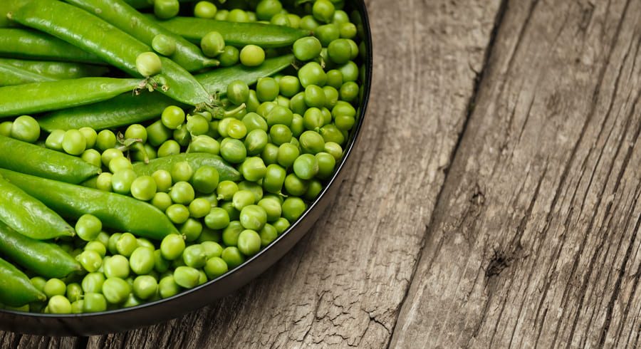 guisantes frescos con vaina sobre mesa de madera, legumbre verde de temporada